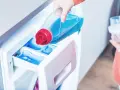 Eine Hand gießt flüssiges Waschmittel in das Fach einer Waschmaschine. So benutzt man eine Waschmaschine richtig.