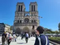 Una persona toma una foto de la fachada de Notre Dame. Mucha gente pasea por la plaza, disfrutando de su visita a Notre Dame.