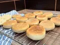 Świeżo upieczone muffiny angielskie, lekko zrumienione, czekają na śniadanie. Dwa przekrojone bułeczki odsłaniają puszyste wnętrze.