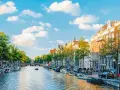 Widok na kanał w Amsterdamie, z łodziami, kamienicami i zielenią. Idealne miejsce na spacer, gdzie jest Amsterdam.