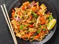 Talerz pełen Pad Thai: makaron ryżowy, tofu, papryka, cebula, groszek i kolendra. Idealny sposób, by dowiedzieć się, pad thai co to.