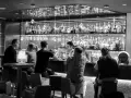 Gente en un bar cine, con un camarero sirviendo bebidas detrás de la barra llena de botellas.