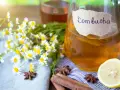 Bouteille de kombucha ambré, décorée de camomille, d'anis étoilé, de bâtons de cannelle et d'une tranche de citron.