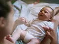 Płaczliwe niemowlę w białym body, trzymające mamę za rękę. Co robić, gdy pojawia się histeria u niemowlaka?