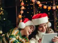 Dos niños con gorros de Santa Claus disfrutan de la tablet, felices cuando dan vacaciones de Navidad, rodeados de luces festivas y un árbol.