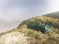 Grön tält och cyklar på en gräsbevuxen sanddyn vid havet. En idyllisk plats för äventyr i sanddynerna Danmark.