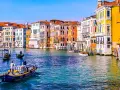 Venezia: turisti in gondola e vaporetti sul Canal Grande, tra palazzi colorati e acque azzurre.