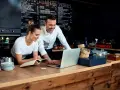 Pareja revisa menú en laptop, planificando su negocio de hostelería en España.