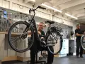 Mekaniker arbetar med en elcykel i verkstad. Verktyg på väggen visar att detta är en plats för bidrag till elcykel.