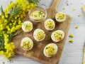 Œufs mimosa garnis d'une sauce crémeuse et de ciboulette, présentés sur une planche en bois avec des fleurs de mimosa. Une recette printanière.