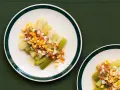 Puerros a la vinagreta servidos en platos blancos con borde verde, cubiertos con una mezcla de tomate picado, huevo duro y perejil.