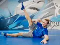 Mężczyzna w niebieskiej koszulce i szarych spodenkach wykonuje ćwiczenie rozciągające na niebieskiej macie.