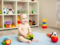 Uśmiechnięte, 8-miesięczne dziecko nie siedzi, bawi się zielonym autkiem na niebieskim kocyku. W tle regał z zabawkami.