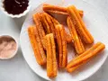 Churros sin gluten espolvoreados con azúcar y canela, servidos con chocolate caliente.