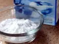 Una ciotola di vetro piena di polvere bianca, probabilmente bicarbonato di potassio, accanto a una scatola blu sfocata.