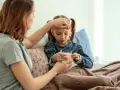 Mutter prüft Fieber bei krankem Kind im Bett. Die Krankschreibung für die Schule ist nötig, damit das Kind sich erholen kann.