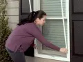 Woman demonstrates how to replace screen door mesh on a window.