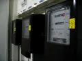 Szereg liczników energii elektrycznej, każdy z wyświetlaczem pokazującym zużycie. Jeden z nich ma żółtą naklejkę z napisem "silnik inwerterowy".
