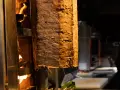 Duży pionowy obrotowy grill z mięsem, obok płomienie ognia.