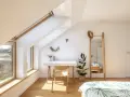 Angolo studio mansardato inondato da la luce più naturale. Scrivania, sedia in legno, specchio alto e pianta.