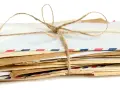 Stos listów w kopertach rozmiar C3, związany sznurkiem. Widać różne rodzaje papieru i ozdobne paski.