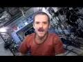 Chris Hadfield singt "Space Oddity" in der ISS. Sein Gesicht mit Schnurrbart ist im Vordergrund, der Raumschiff-Innenraum im Hintergrund.