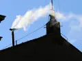 Biały dym z komina, jak sygnał wyboru nowego papieża, unosi się na tle błękitnego nieba.