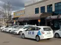 Reihe weißer Taxis vor einem Gebäude mit Taxischildern.