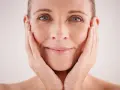 Visage d'une femme aux mains sur les joues, montrant les signes du temps et les défis des problèmes de peau et ménopause.