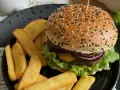 Soczysty burger z sezamem i frytki na czarnym talerzu.