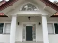 Elegancki pilaster zdobi fasadę domu, wspierając dach nad wejściem. Obok okna i drzwi, tworzy klasyczną kompozycję.