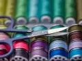 Ciseaux sur une rangée de bobines de fil à coudre aux couleurs vives. Le grosseur de fil à coudre varie, offrant un arc-en-ciel de possibilités créatives.