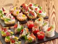 Varietà di tartine, involtini e pomodorini ripieni, perfette per idee aperitivo economico e gustoso.