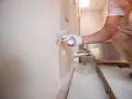 Ręka w rękawicy nakłada tynk kornik na ścianę za pomocą kielni.
