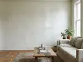 Soggiorno con divano beige, tavolino in legno e piante. Le pareti bianche mostrano segni del tempo, suggerendo che è ora di pensare a ogni quanto imbiancare casa.