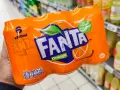 Opakowanie 6 puszek Fanty Orange w ręce, na tle sklepowych półek z napojami.