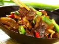 Chopsticks podnoszą kawałek aromatycznej wołowiny po chińsku z miski pełnej pysznego dania z warzywami.