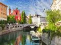 Urokliwy kanał w Lublanie, Słowenia, z łodzią wycieczkową i mostem w tle.