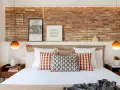 Ideas para decorar la pared de la cabecera de la cama: ladrillo visto, cuadros y lámparas naranjas.