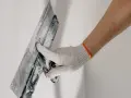 Mano enguantada alisando masilla para tapar agujeros en la pared.