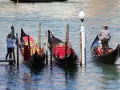 Gondole veneziane ornate, una turista scatta foto. La differenza tra gondola e sandalo è chiara: una naviga, l'altro si indossa.