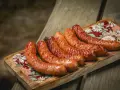 Apetyczna kiełbasa z grilla, rumiana i soczysta, ułożona na drewnianej desce z kolorowym wzorem.
