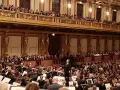 Un director dirige una orquesta sinfónica ante un público entusiasta, interpretando obras de Beethoven en un teatro majestuoso.