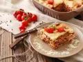 Pyszna, wielowarstwowa lasagne z mięsem mielonym, polana sosem beszamelowym i posypana parmezanem. Na talerzu ozdobiona pomidorkami koktajlowymi i bazylią.