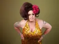 Osoba w złotej, cekinowej sukience i peruce, z kwiatem we włosach. To przykład tego, co to jest drag queen – artystyczna forma ekspresji.