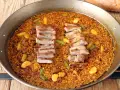 Arroz con secreto, un plato de paella con cerdo tierno y verduras crujientes, listo para ser disfrutado.