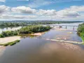 Szeroka rzeka z piaszczystymi łachami i zielonymi wyspami, przecinana mostem. To krajobraz Wisły, najgłębszej rzeki w Polsce, w słoneczny dzień.