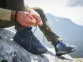 Uomo lega i lacci di scarponi da hiking su roccia, pronto per il trekking in montagna.