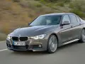 Szary sedan BMW F30 z dynamicznymi silnikami pędzi po drodze, ukazując sportowy charakter.