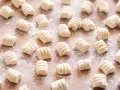 Gnocchi di ricotta freschi, pronti per essere cucinati, spolverati di farina su un tagliere di legno.